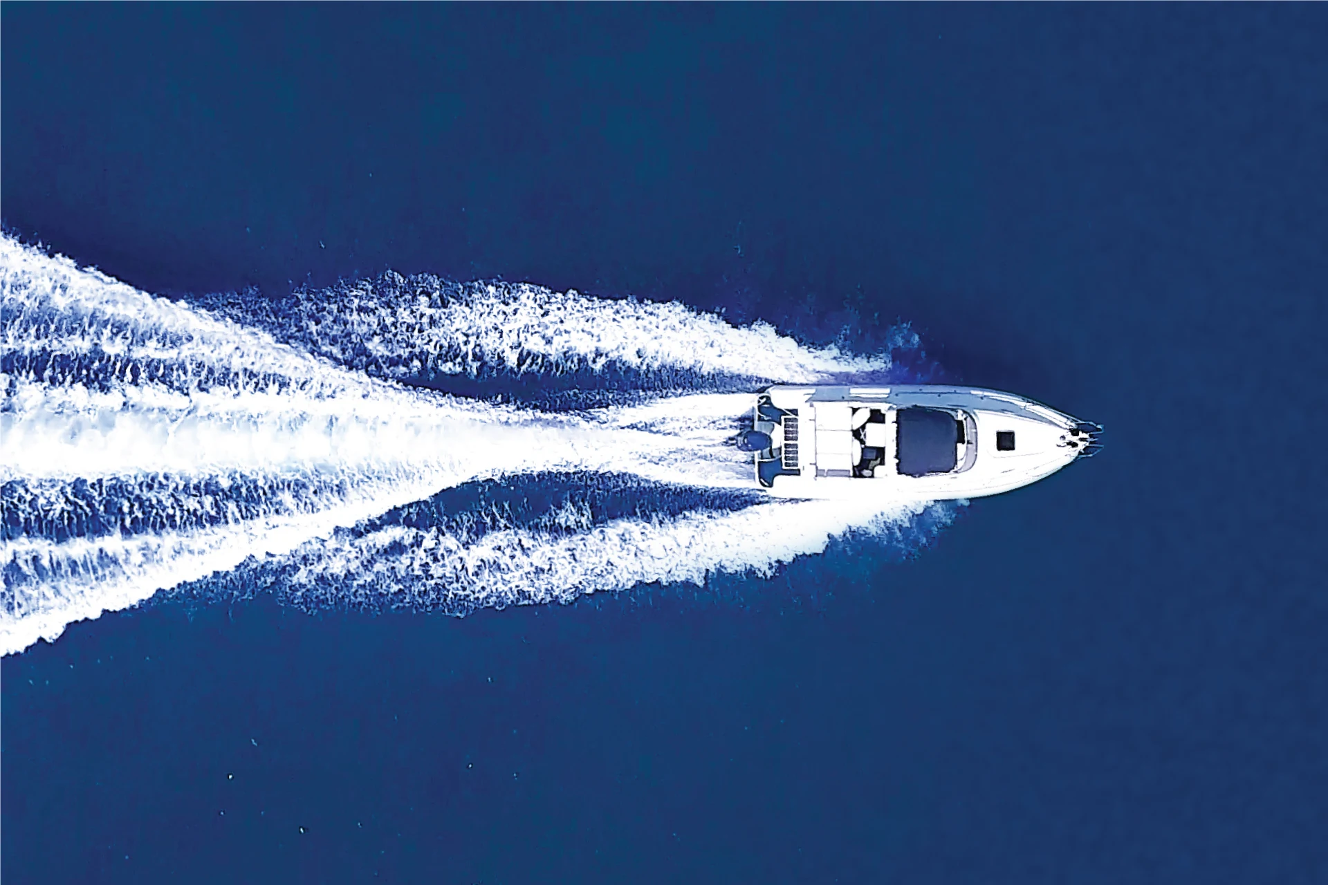 Aerial view of a boat navigating through water, creating wake patterns.