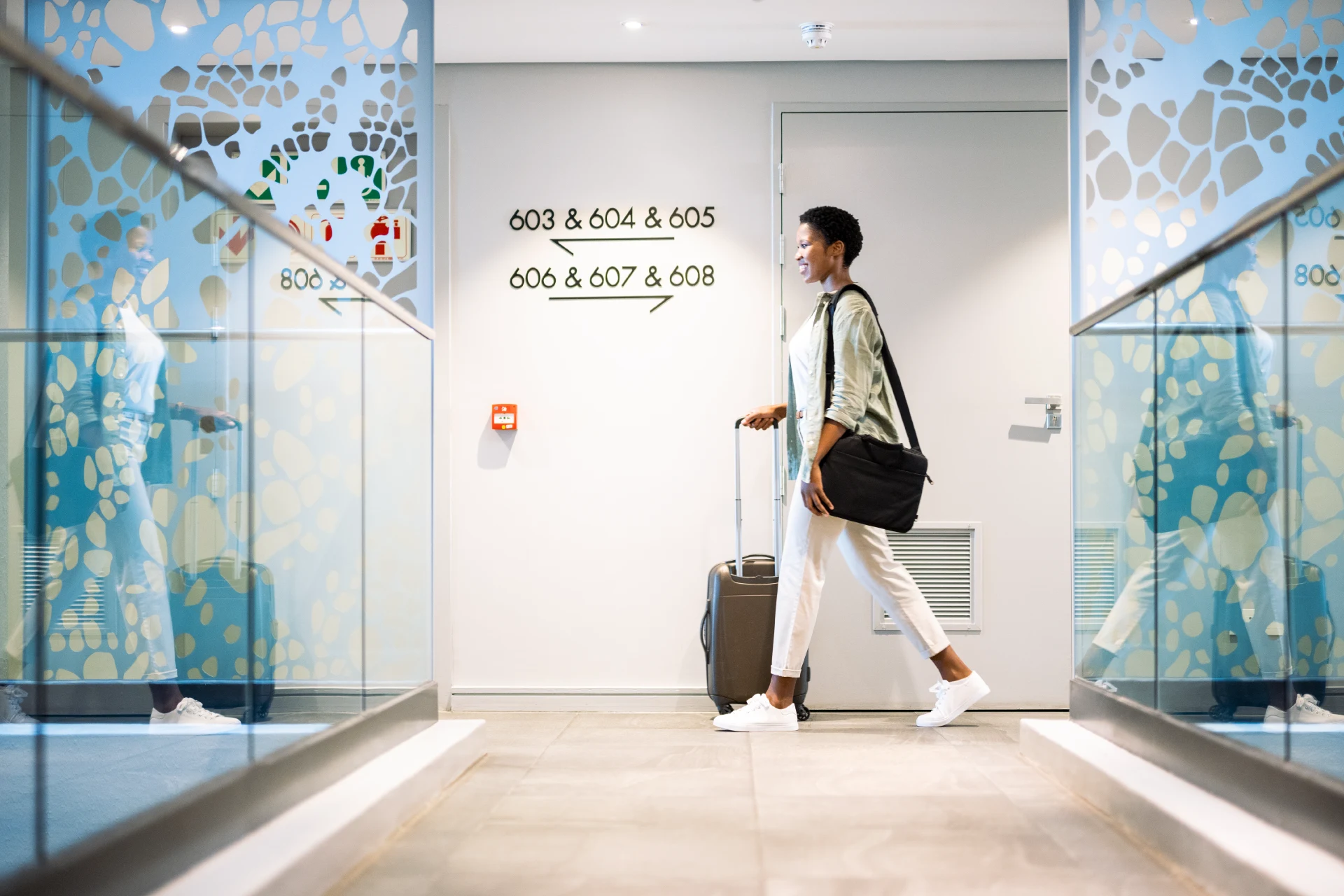 Person walking with luggage in a hotel corridor towards room numbers