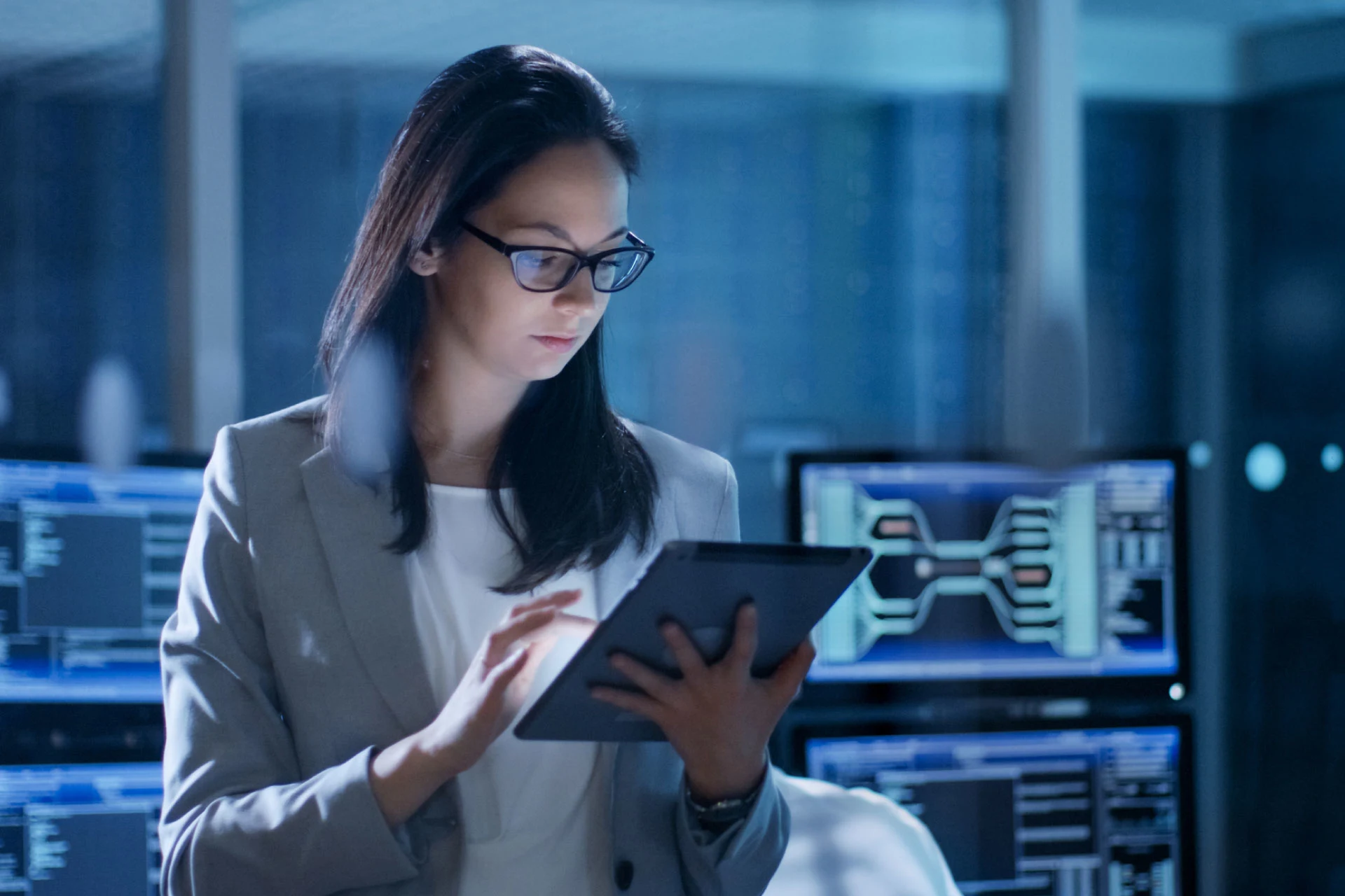 Professional using a tablet in a tech environment with multiple monitors.