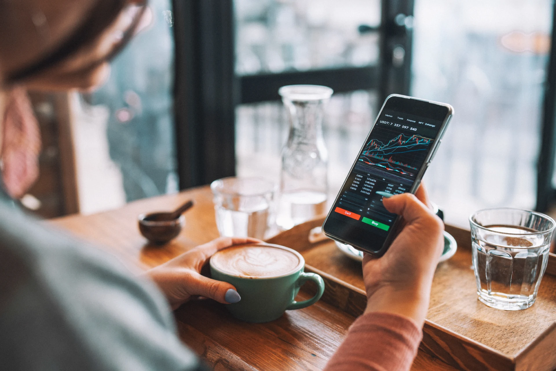 User checking a trading application on a smartphone while enjoying coffee.