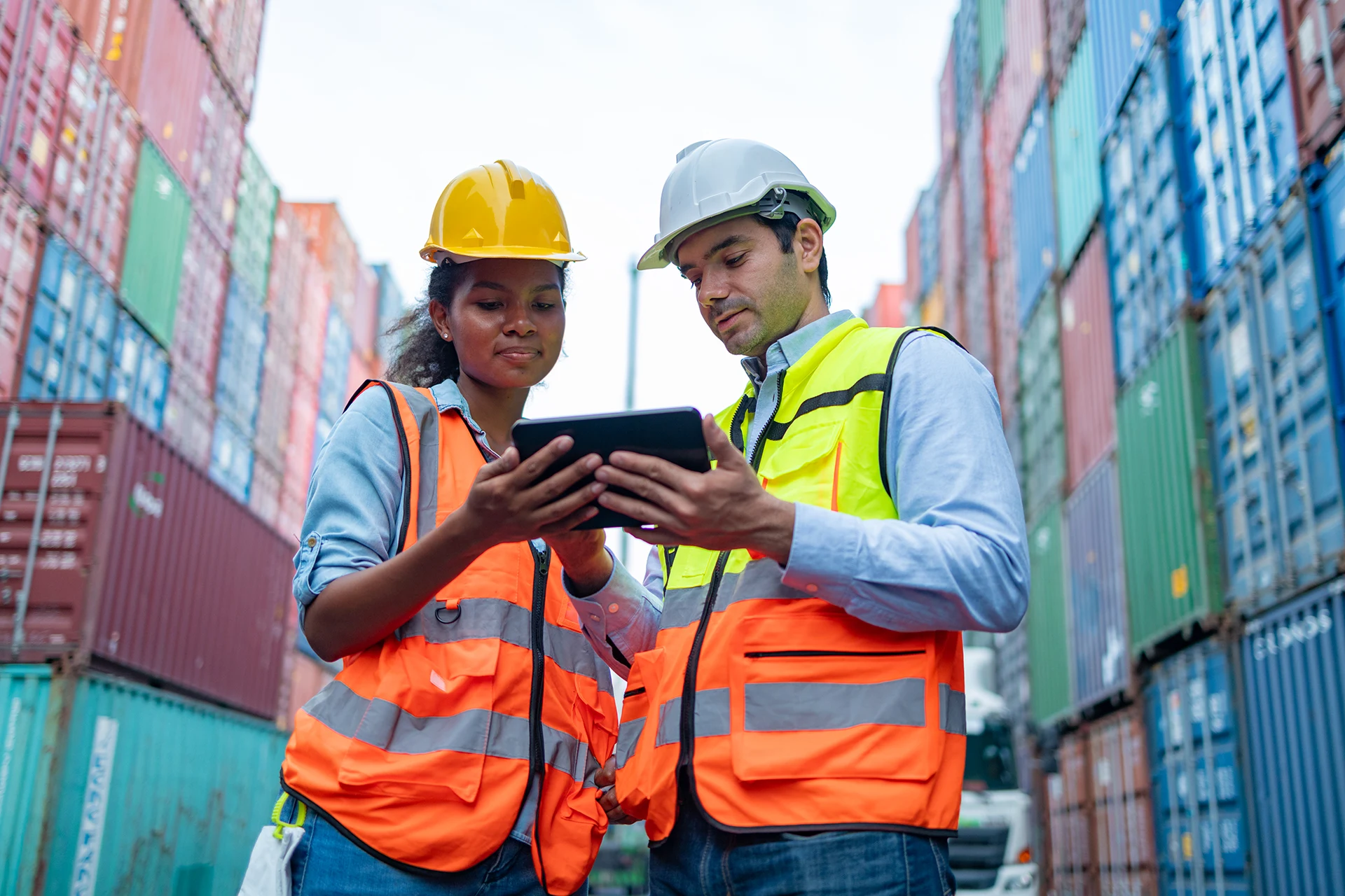 Two logistics professionals reviewing data on a tablet amid shipping
