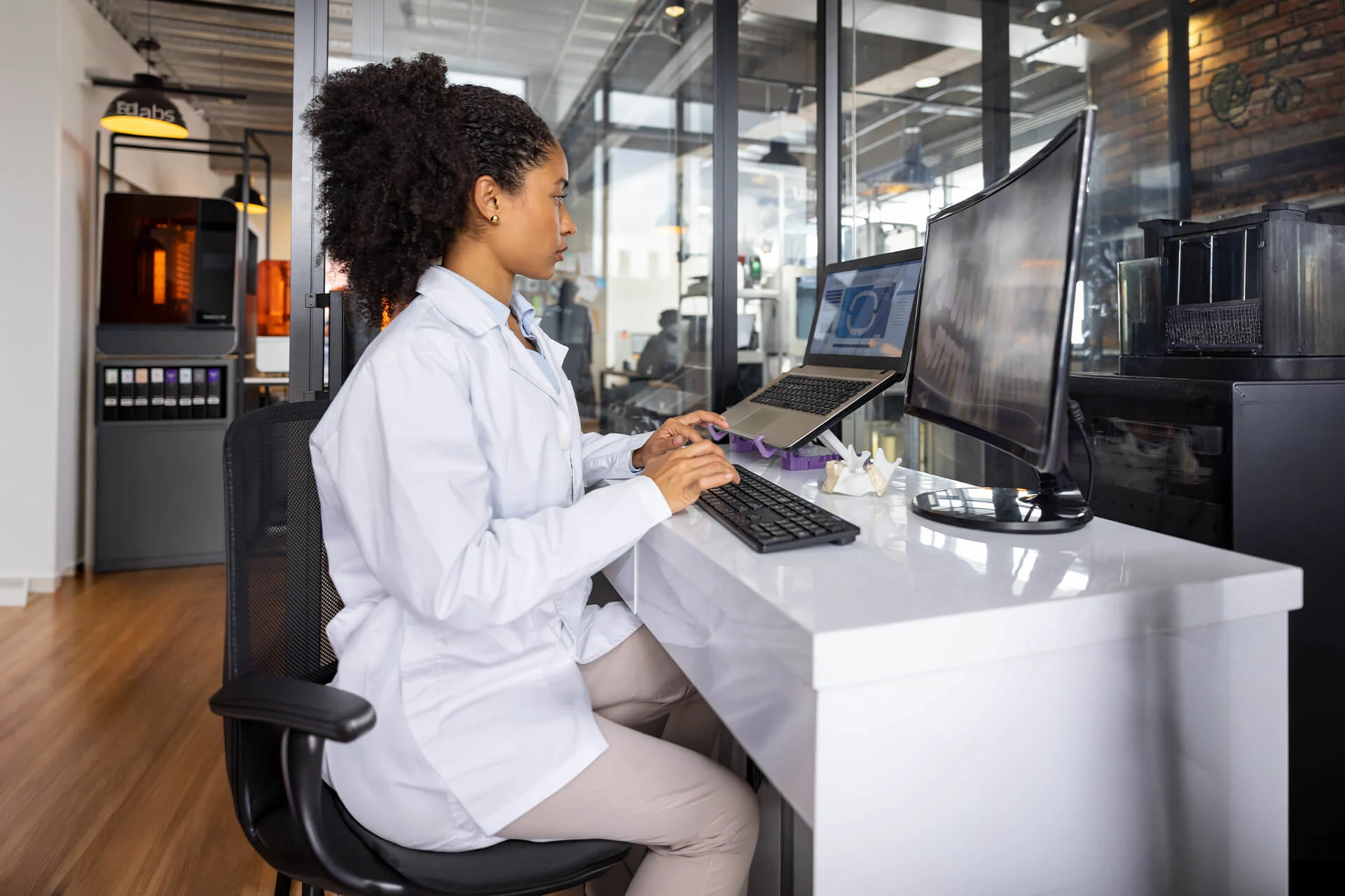 Woman in lab coat typing on laptop at a modern workspace in healthcare