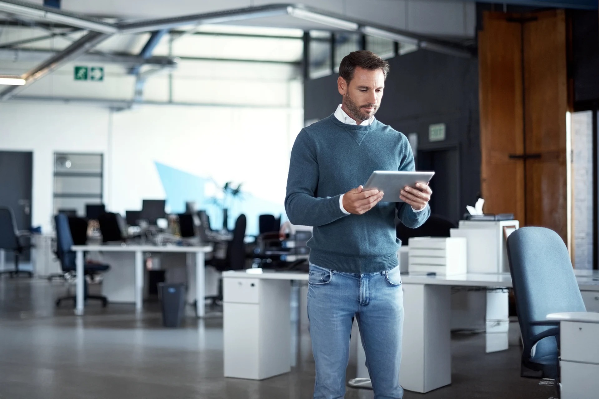 Employee standing in a workspace reviewing data on a tablet, representing enterprise applications and cloud-based application services