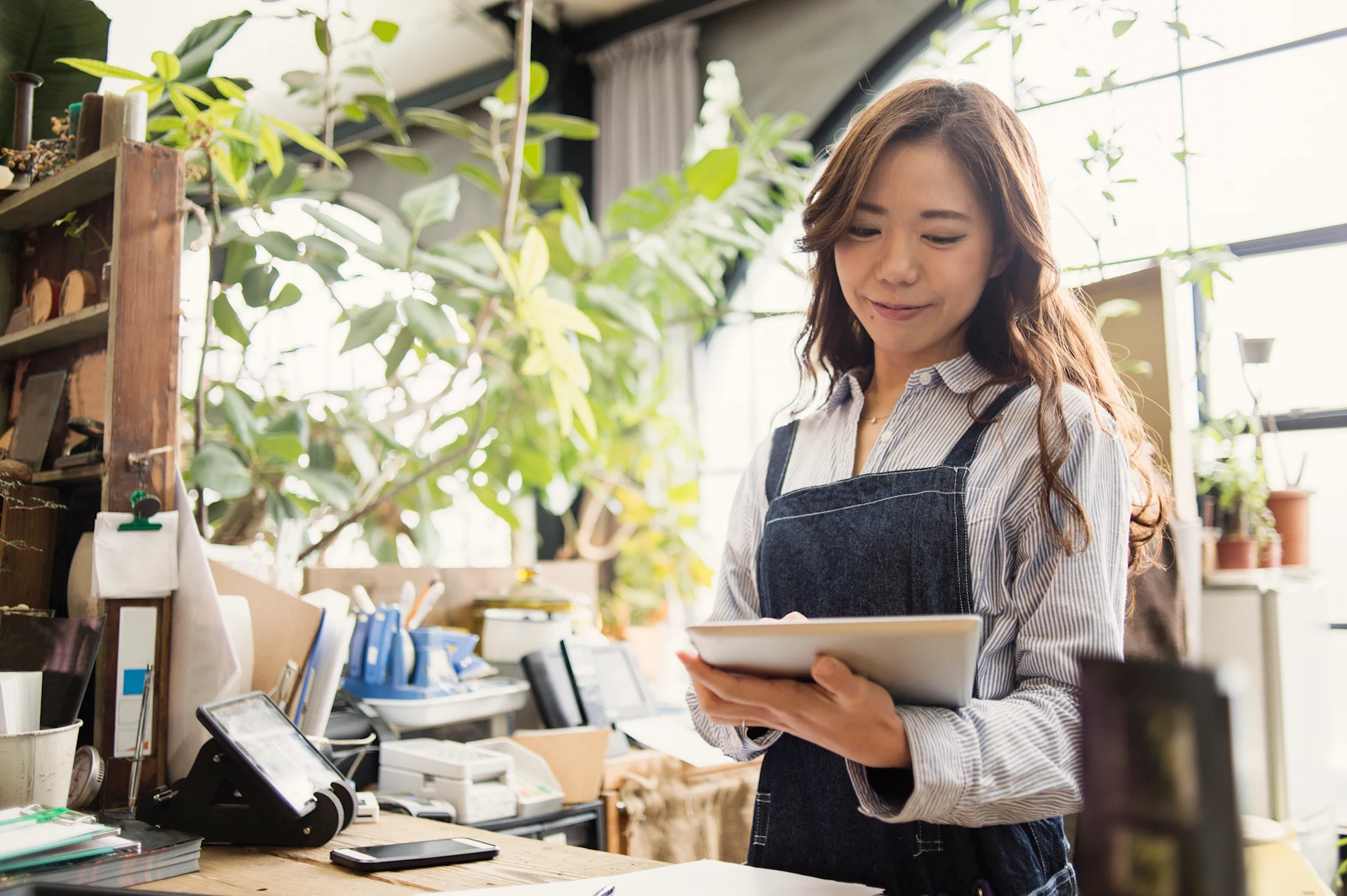 Woman holding a tablet in a retail workspace with plants around.
