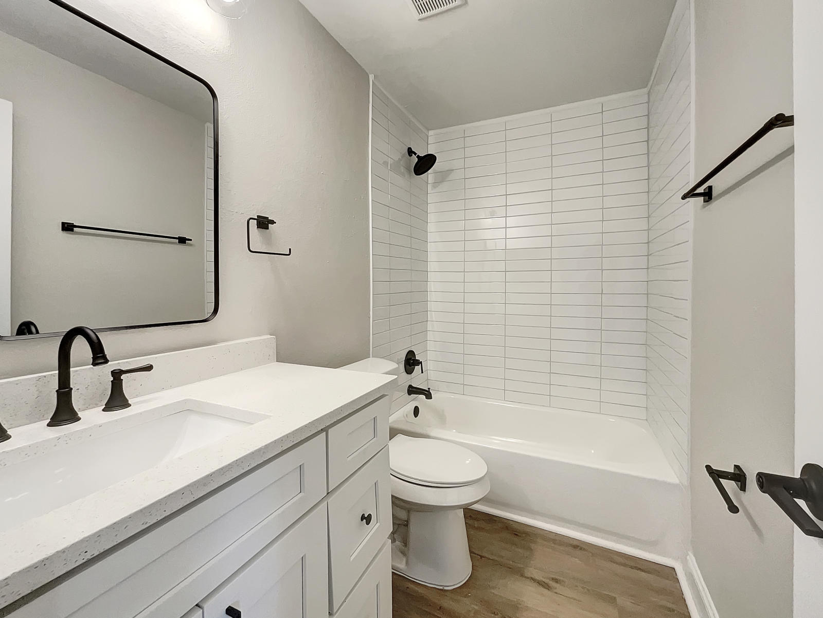 This bathroom in Tampa is brightened up with luxury-vinyl plank floors, white subway shower tile, and matte black faucets.