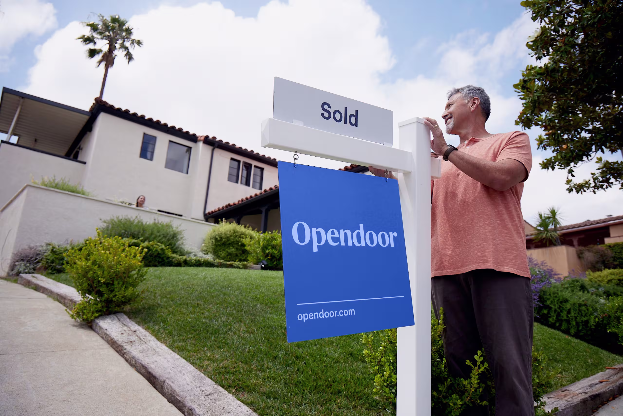 A man standing new to an Opendoor "Sold" sign and looking satisfied.
