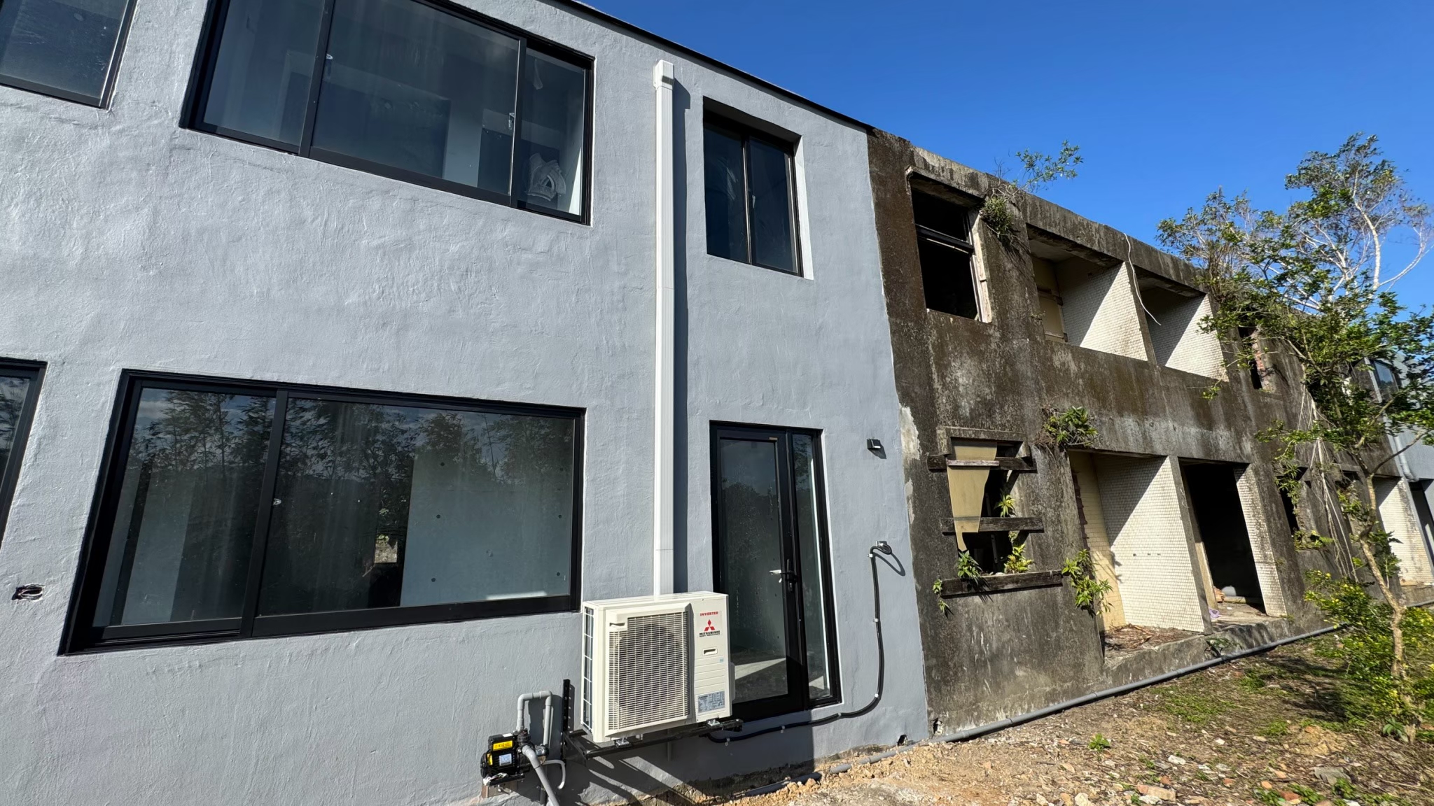 建築左側已完成翻新並裝上三菱重工空調室外機，右側仍保留原始廢墟樣貌，商業空間空調規劃從廢墟階段即進場