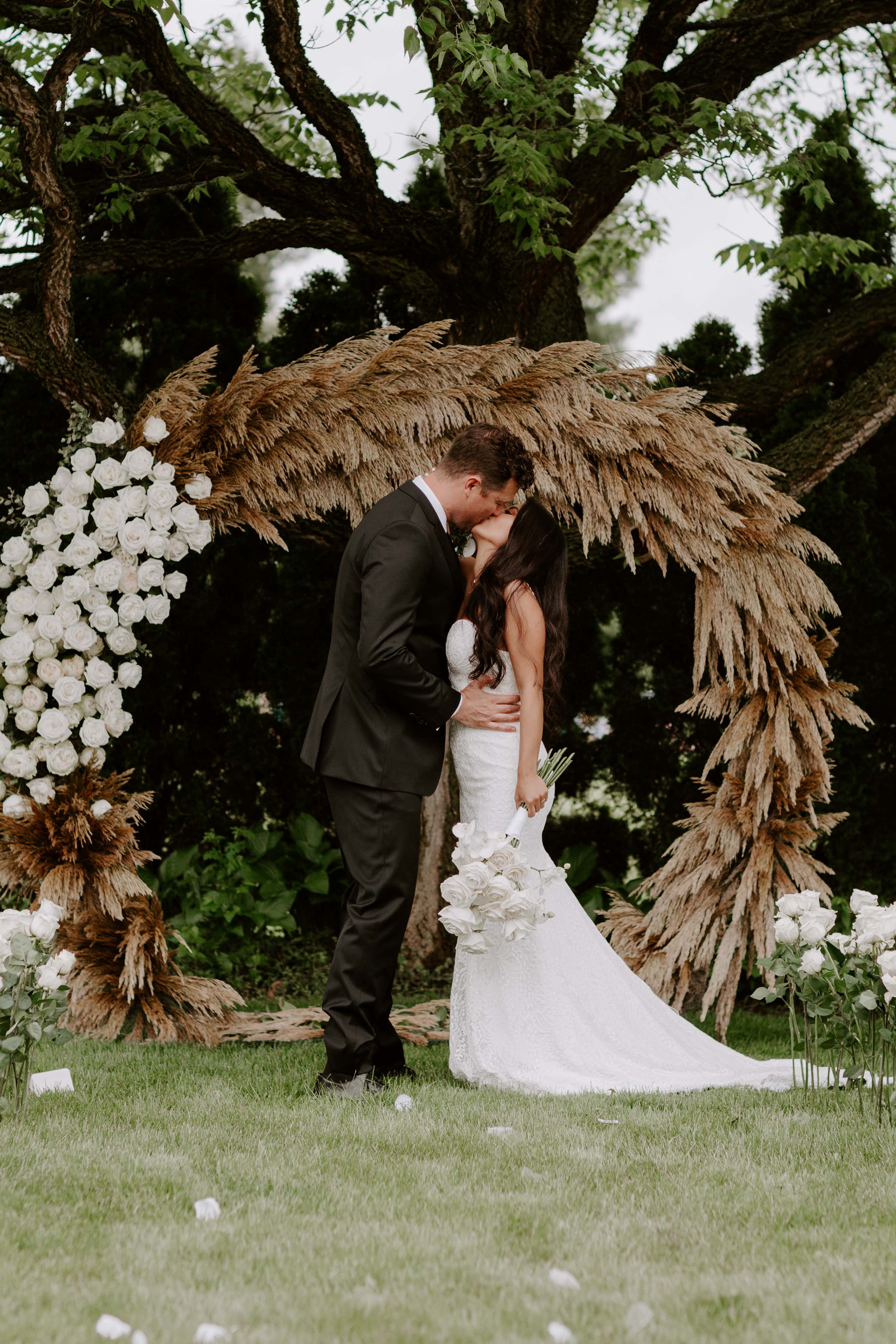 bride and groom having first kiss under floral wedding arch