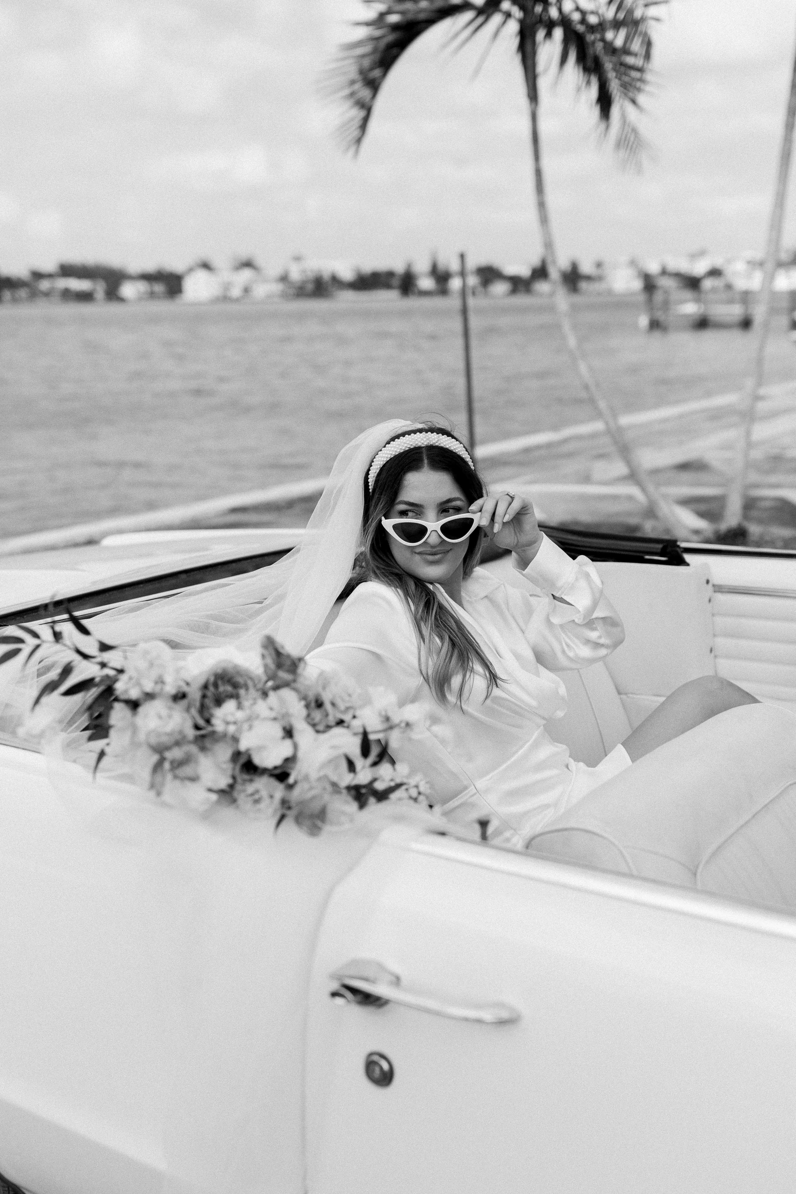 Black and white photo of bride holding bouquet in getaway car