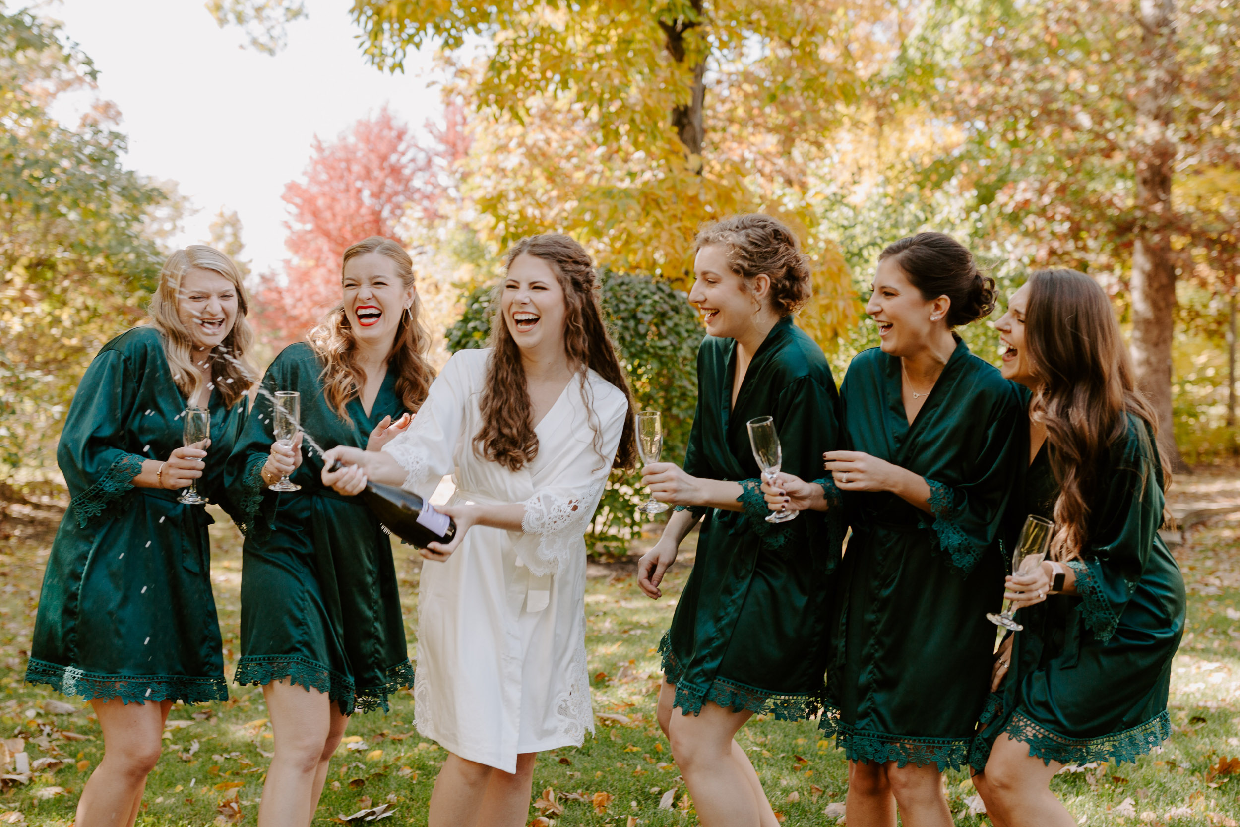 Bride popping champagne with bridesmaids wearing matching green robes