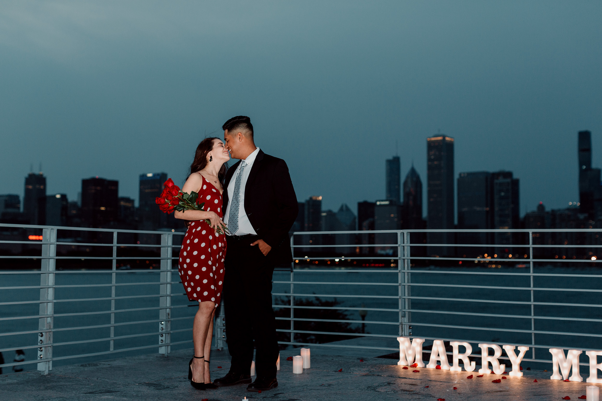 Marry me sign and engaged couple against Chicago skyline with a bouquet of roses | Chicago Skyline Proposal | Proposal Ideas | Chicago Engagement Photographer | Chicago Proposal Photographer | Chicago Proposal | Proposal Stories | How to Propose | She Said Yes | Engaged | Places to Get Engaged in Chicago