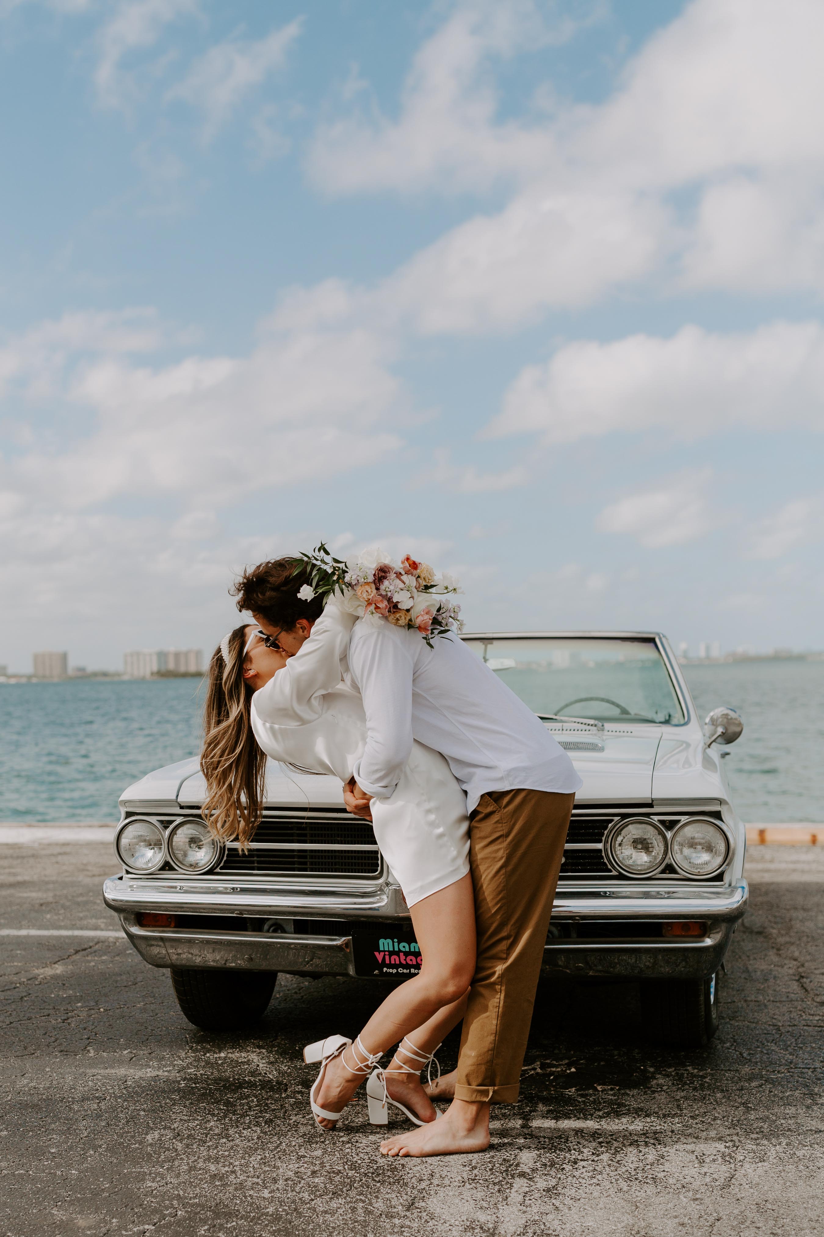 Bride and groom posing in front of vintage white car