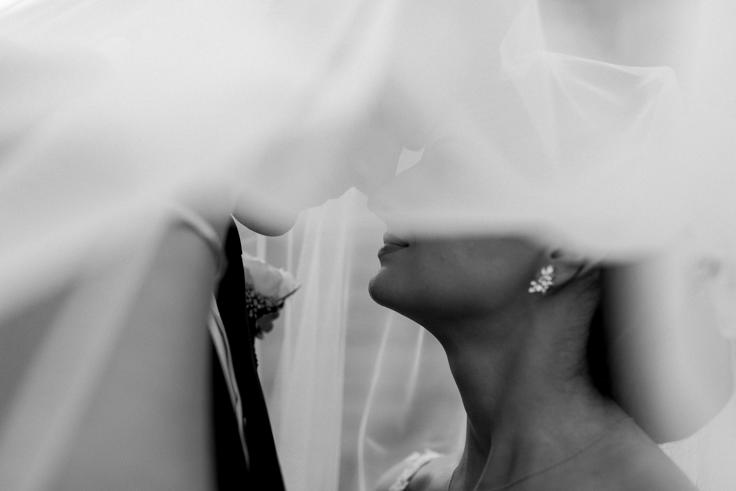 Black and white photo of bride and groom under veil