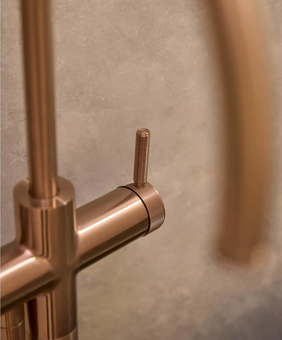 Close-up of a bronze bathroom floor-mounted faucet with textured handle against a neutral beige wall.