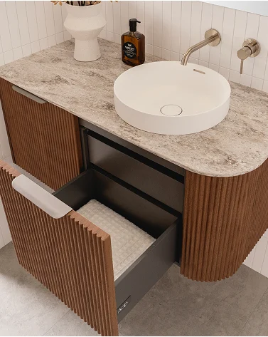 Modern bathroom vanity with marble countertop, white circular sink, wooden ribbed cabinet, and open drawer.