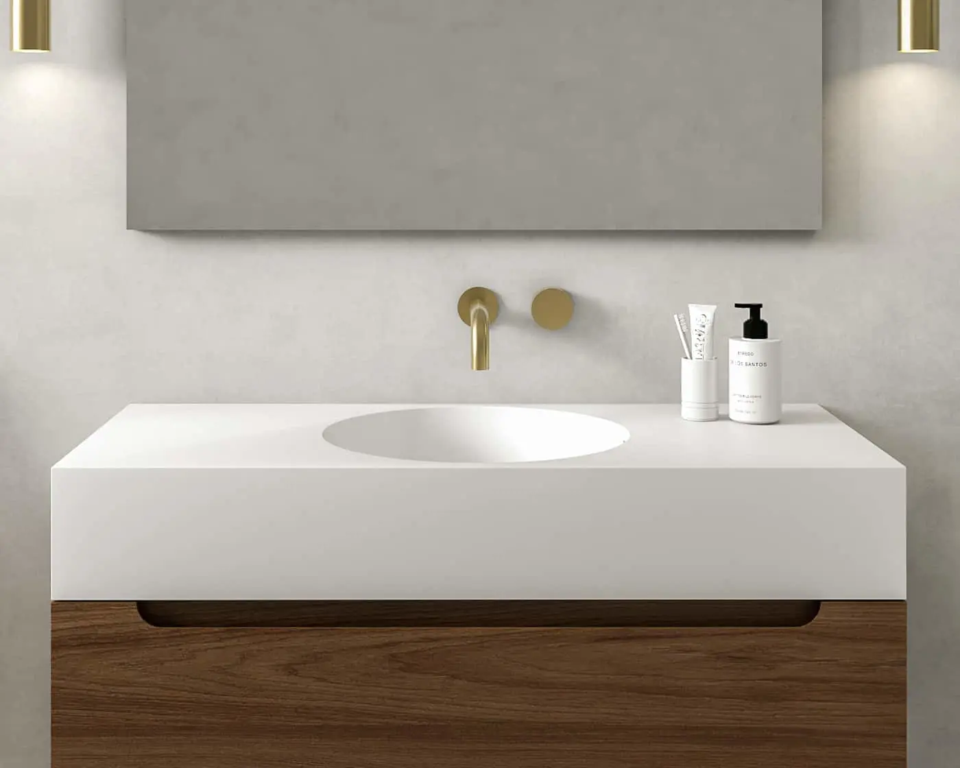 Minimalist bathroom sink with white countertop, brass wall-mounted faucet, wooden cabinet, and toiletry products.