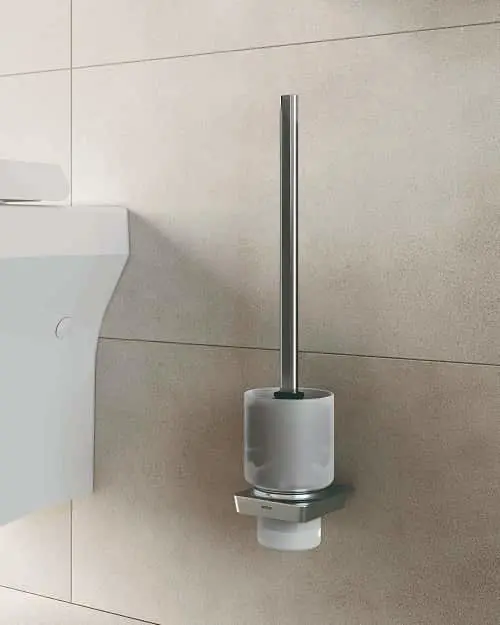 Modern wall-mounted toilet brush with cylindrical gray holder and chrome handle against beige tiled bathroom wall.