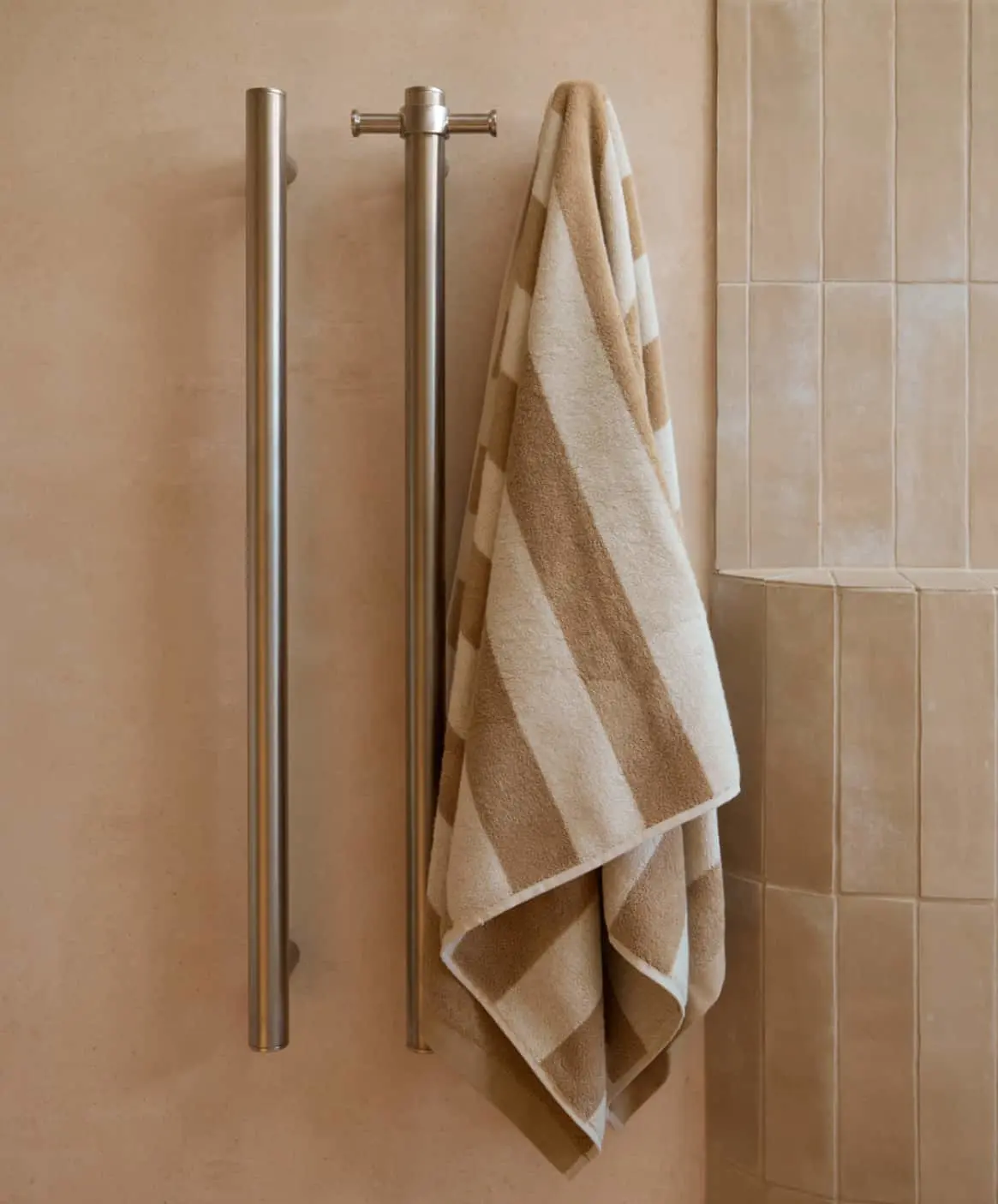 Beige and white striped towel hanging on a stainless steel towel bar in a bathroom with neutral-colored tile walls.