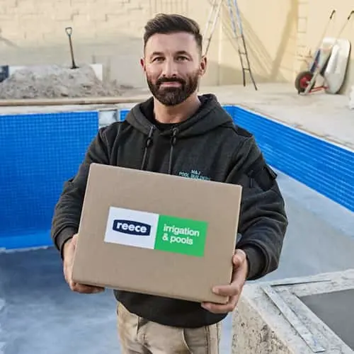Person in black hoodie holding a cardboard box labeled "Reece Irrigation & Pools" next to an empty blue pool.