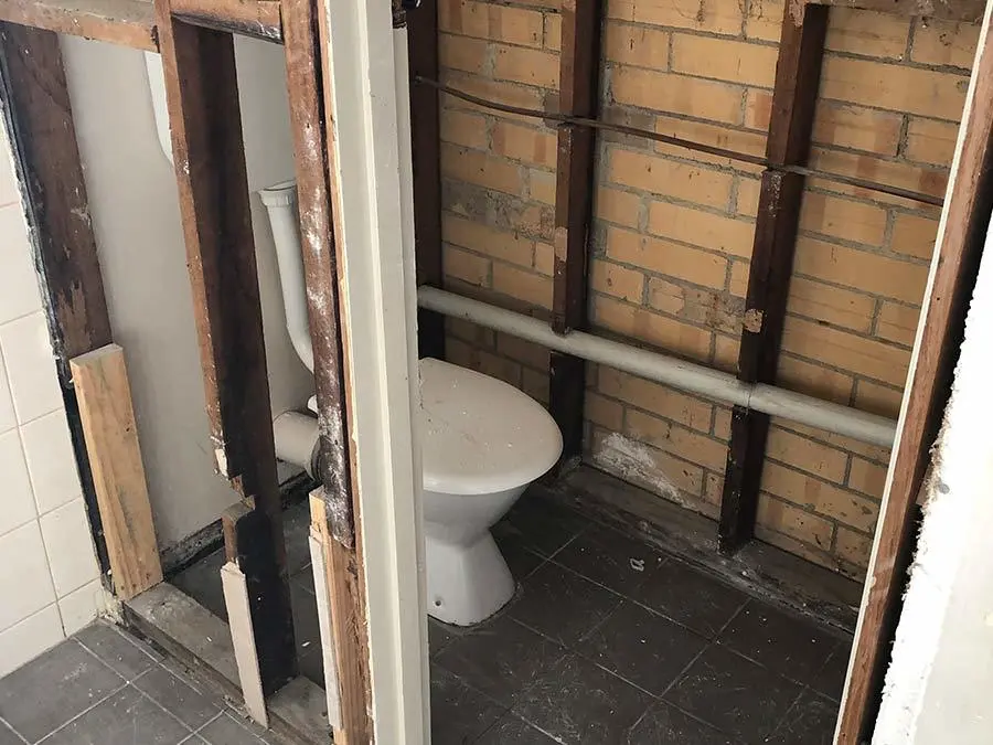 Bathroom under renovation with exposed brick walls, wooden framing, and a white toilet in the center.