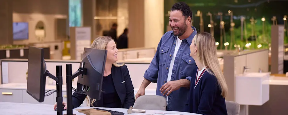 Three people having a friendly conversation at a retail counter with computer monitors in a modern store environment.