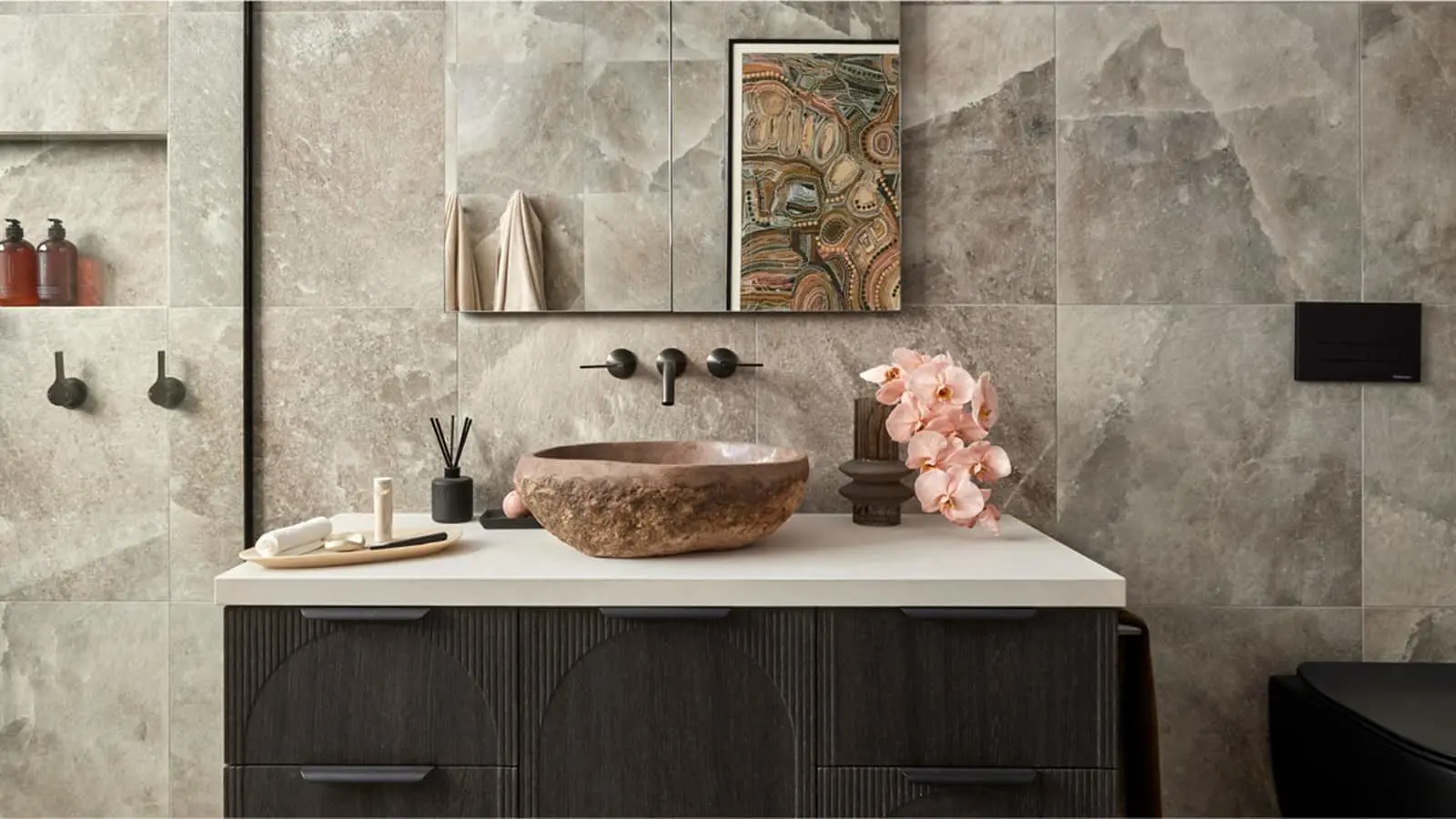 Modern bathroom with stone vessel sink, dark wood vanity, marble walls, mirror cabinet, and pink orchids.