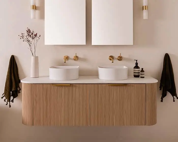 Modern bathroom with dual white vessel sinks on wooden vanity, brass fixtures, and minimalist beige decor.