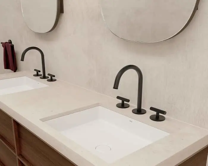 Modern bathroom vanity with dual white sinks, black curved faucets, and round mirrors on a cream wall.