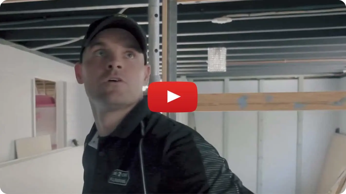 Person in dark clothing and cap in construction area with YouTube play button overlay