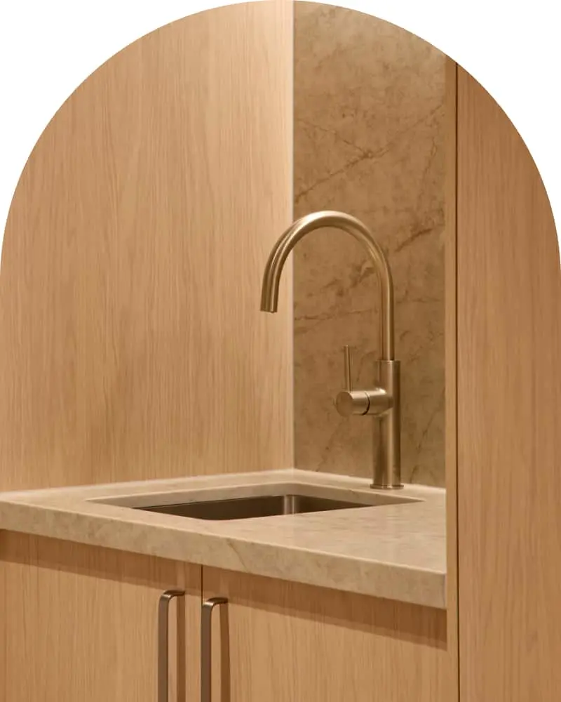 Modern kitchen sink with brass faucet set in light wood cabinetry.