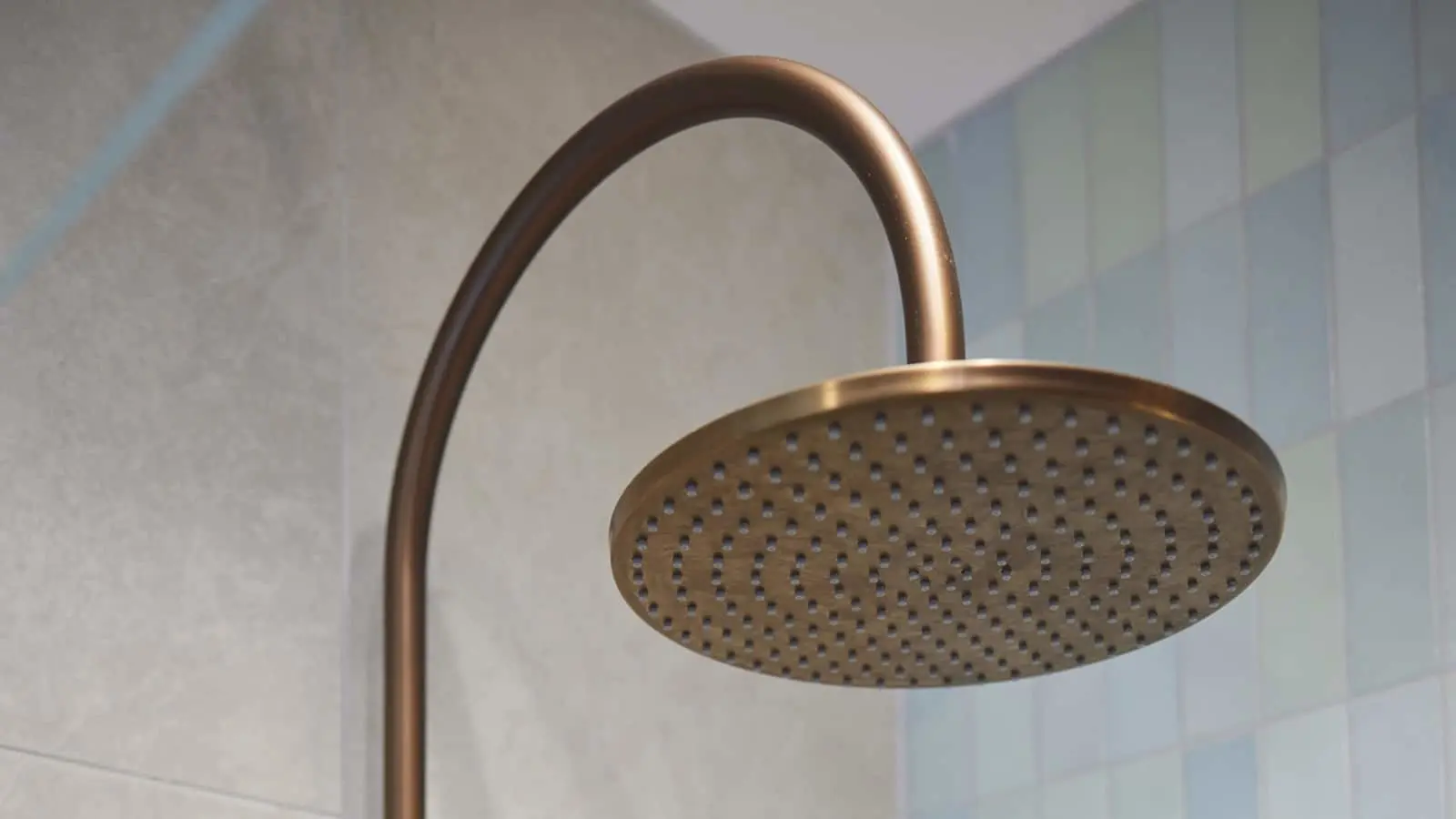 Bronze rainfall shower head with curved arm mounted on white tiled bathroom wall.