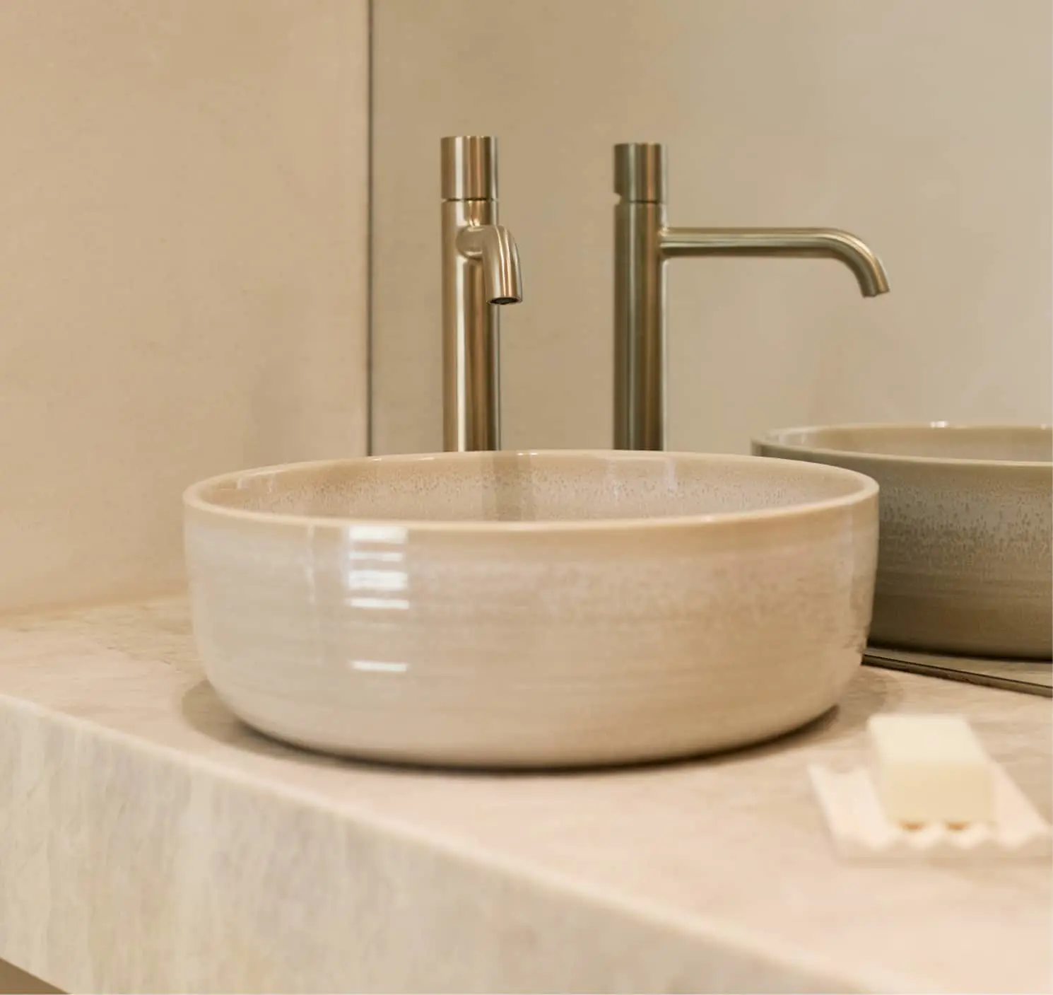 A round ceramic vessel sink in cream glaze on a stone countertop with a tall brushed nickel faucet behind it.