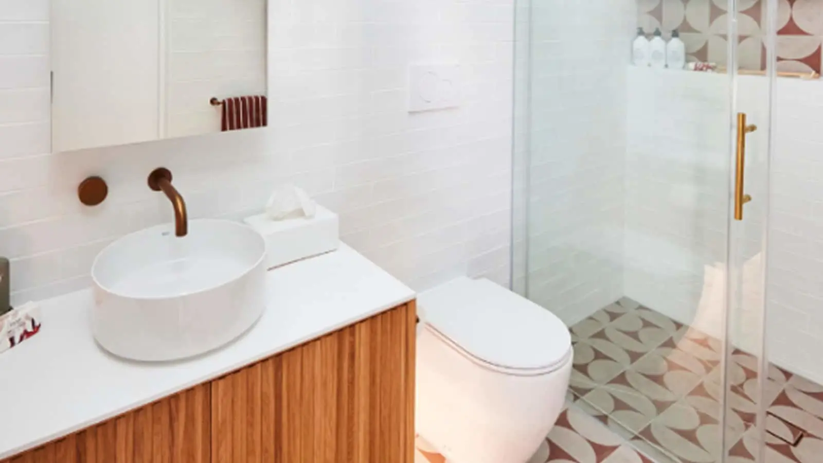 Modern bathroom with white vessel sink, wooden vanity, white toilet, glass shower door, and patterned floor tiles.