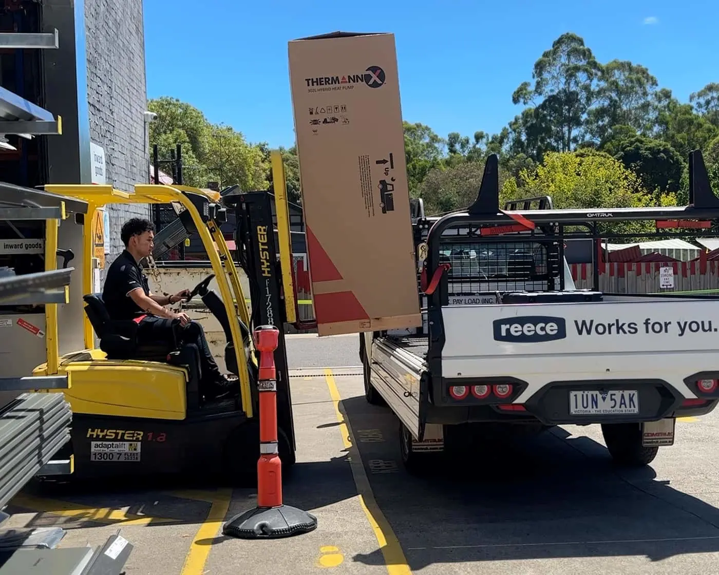 Worker operating yellow Hyster forklift loading a Thermann box onto a Reece utility truck in a loading bay.