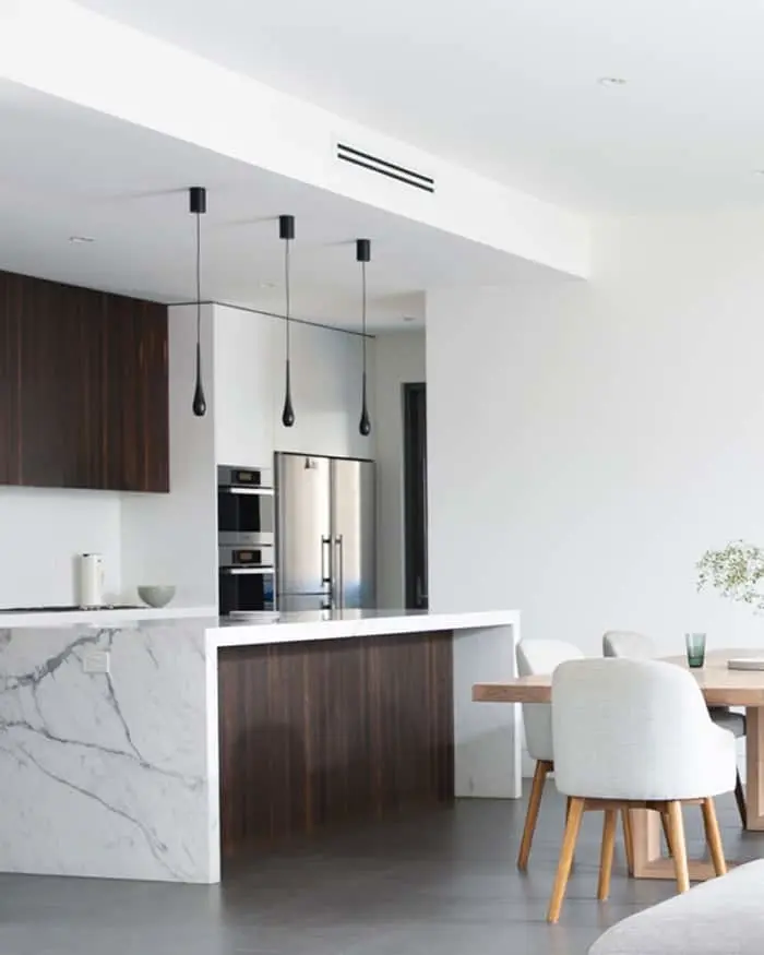 Modern kitchen with marble island, dark wood cabinets, stainless steel appliances, and pendant lights above dining area.