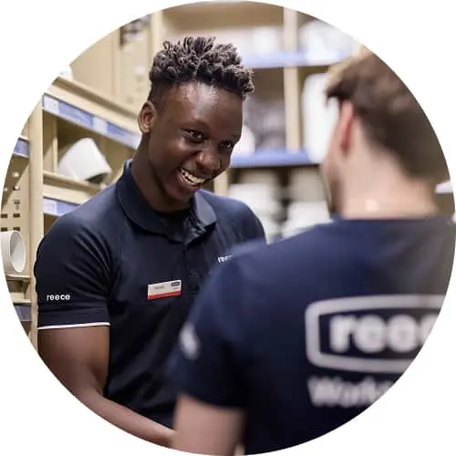 Two colleagues in navy blue Reece uniforms having a conversation in what appears to be a warehouse setting.