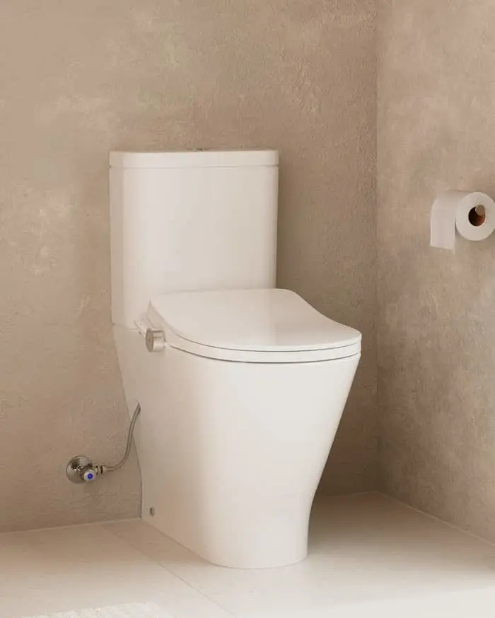 White modern toilet in a bathroom with beige textured walls and toilet paper holder mounted on the wall.
