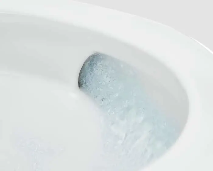 Close-up of a white toilet bowl interior with water flushing and swirling around the rim.