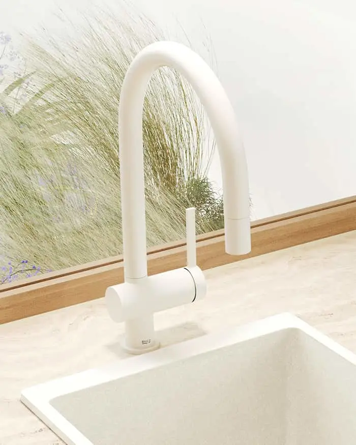 White modern kitchen faucet with high curved spout over a white sink, against a wall with grass pattern wallpaper.