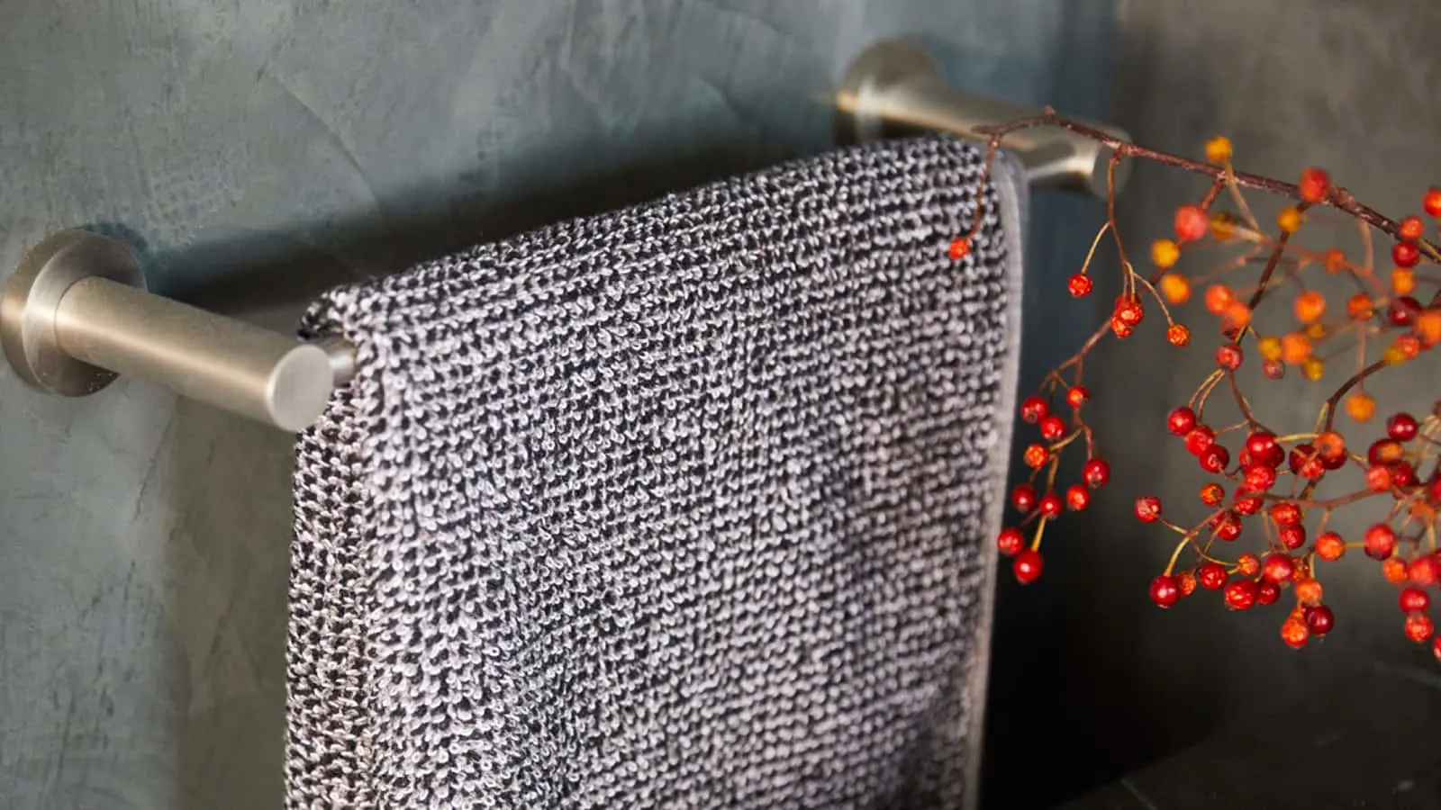 Black and white textured towel hanging on a metal rod with red berries decorating the side against a gray wall.