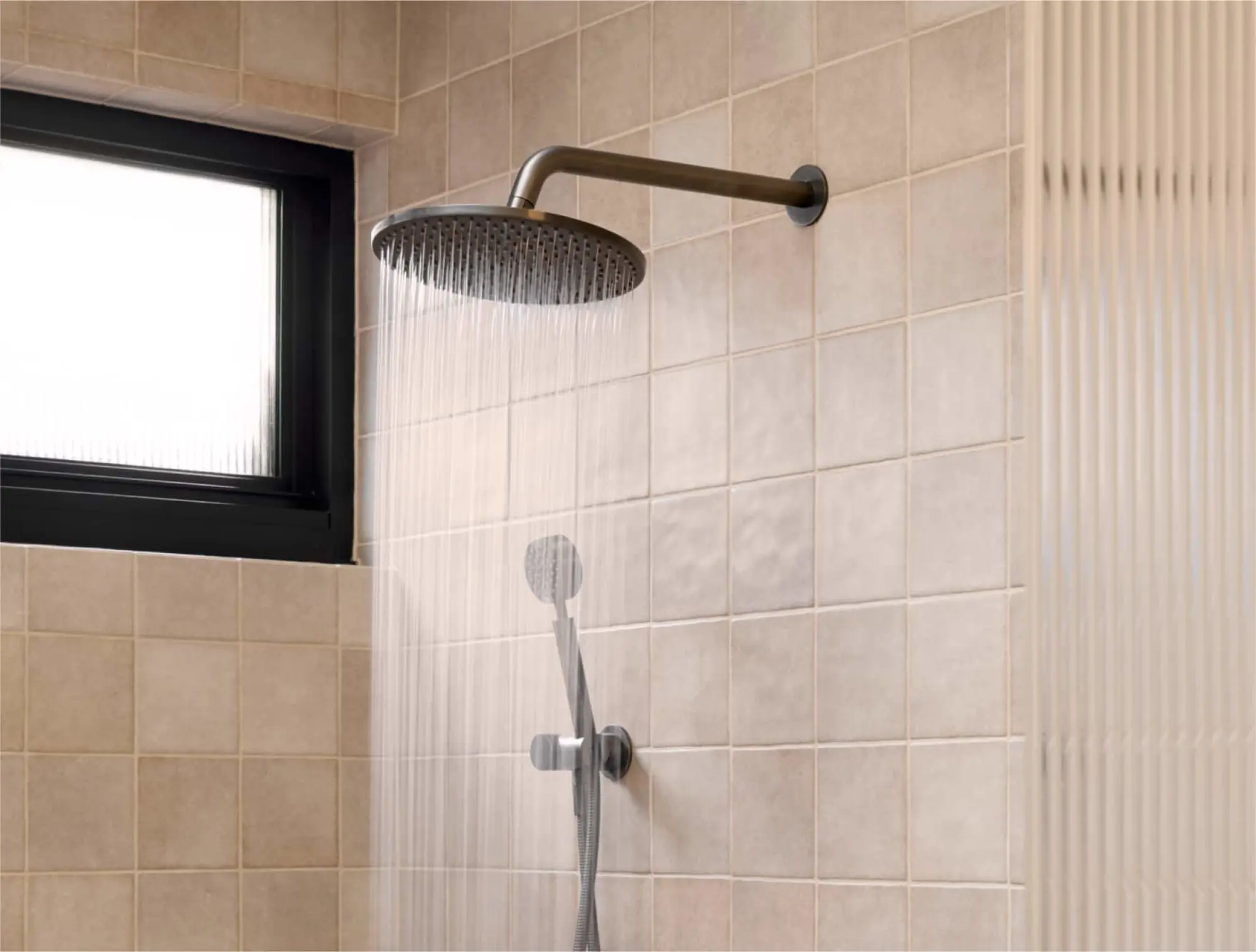 Modern rainfall shower head with water flowing in a beige tiled bathroom with small window.