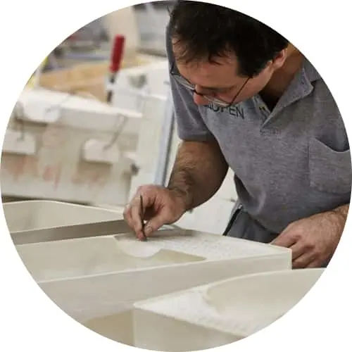 Craftsman in gray shirt carefully working on white bathroom sink or countertop in manufacturing workshop.