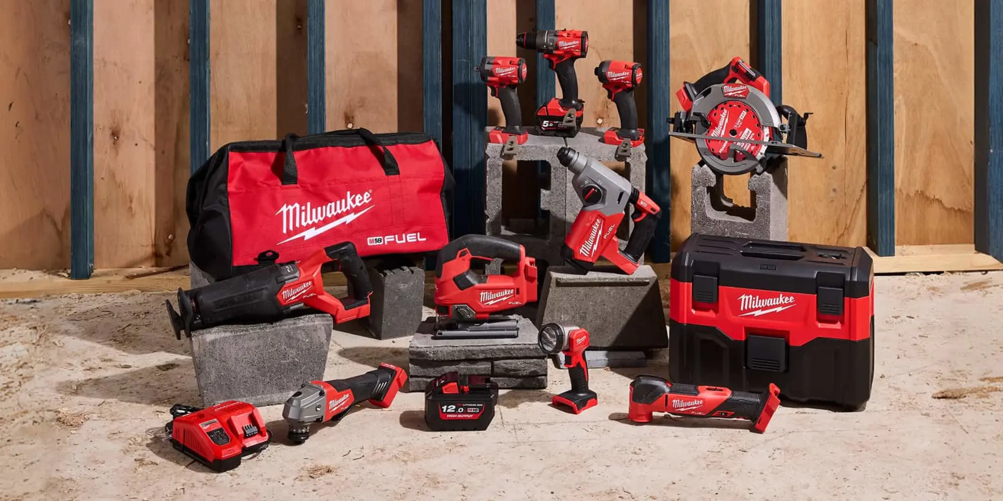 A collection of Milwaukee M18 FUEL cordless power tools displayed on a construction site floor with a red tool bag.