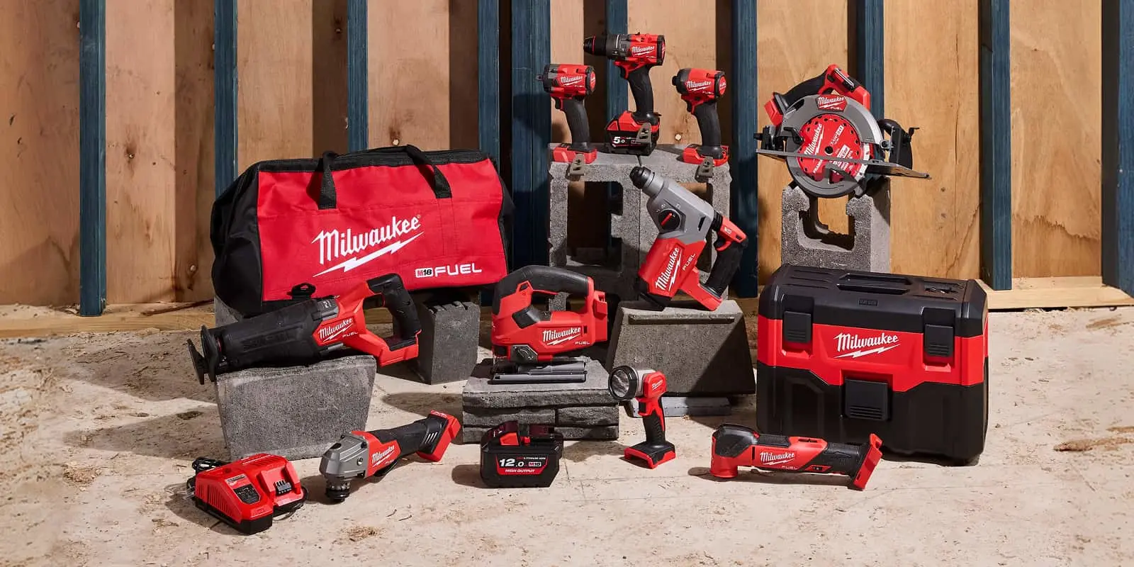 A collection of Milwaukee M18 FUEL cordless power tools displayed on a construction site floor with a red tool bag.