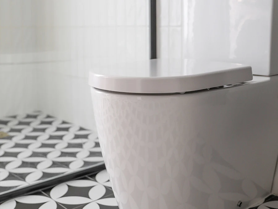 White toilet with closed lid in a bathroom with black and white patterned floor tiles and white walls.