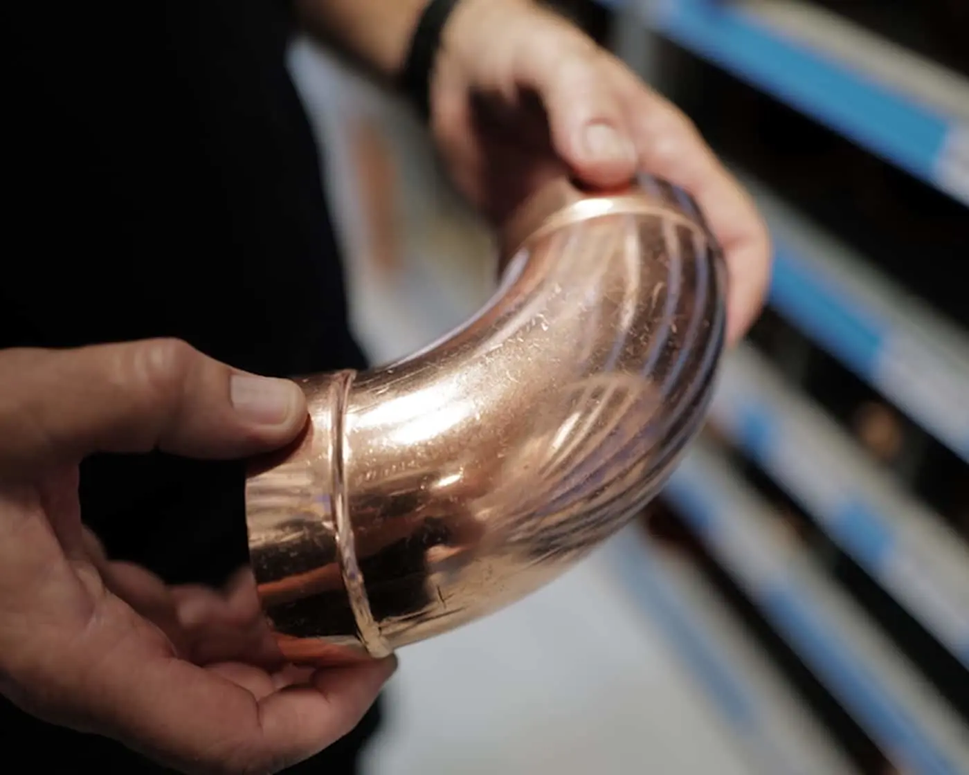 Hands holding a curved copper pipe fitting or plumbing component with a polished, shiny surface.
