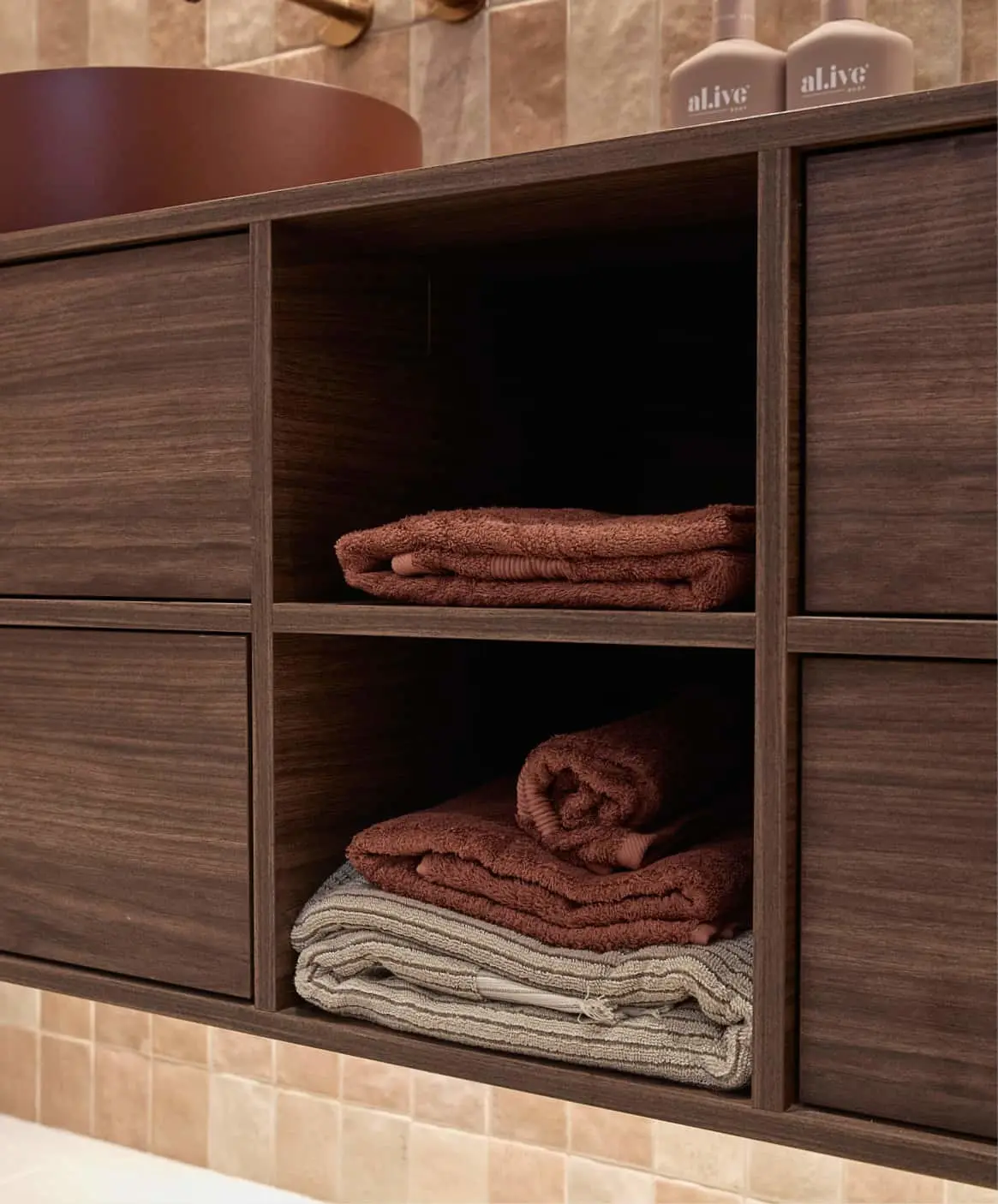 Dark wooden bathroom cabinet with folded rust-colored and beige towels, with skincare products on top.