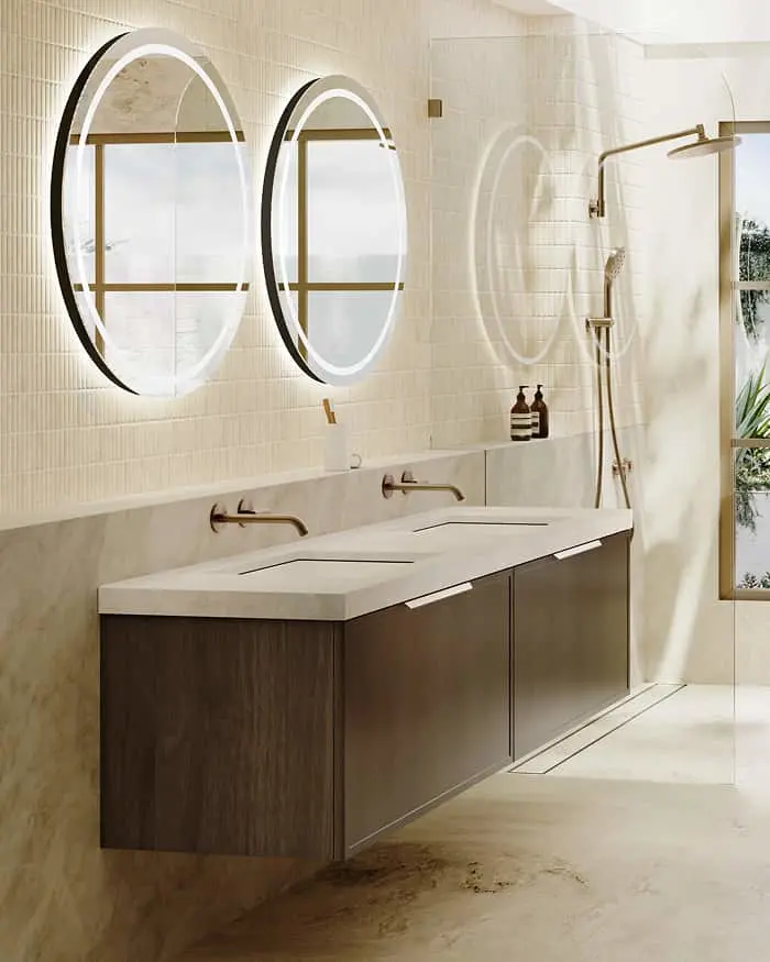 Modern bathroom with floating dark wood vanity, two circular backlit mirrors, brass fixtures, and glass shower enclosure.