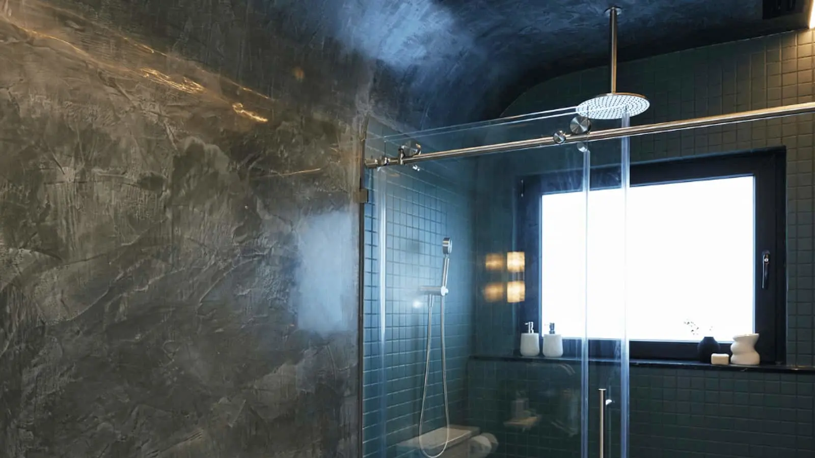 Modern bathroom with dark textured walls, glass shower enclosure, rainfall showerhead, and blue tile accents.