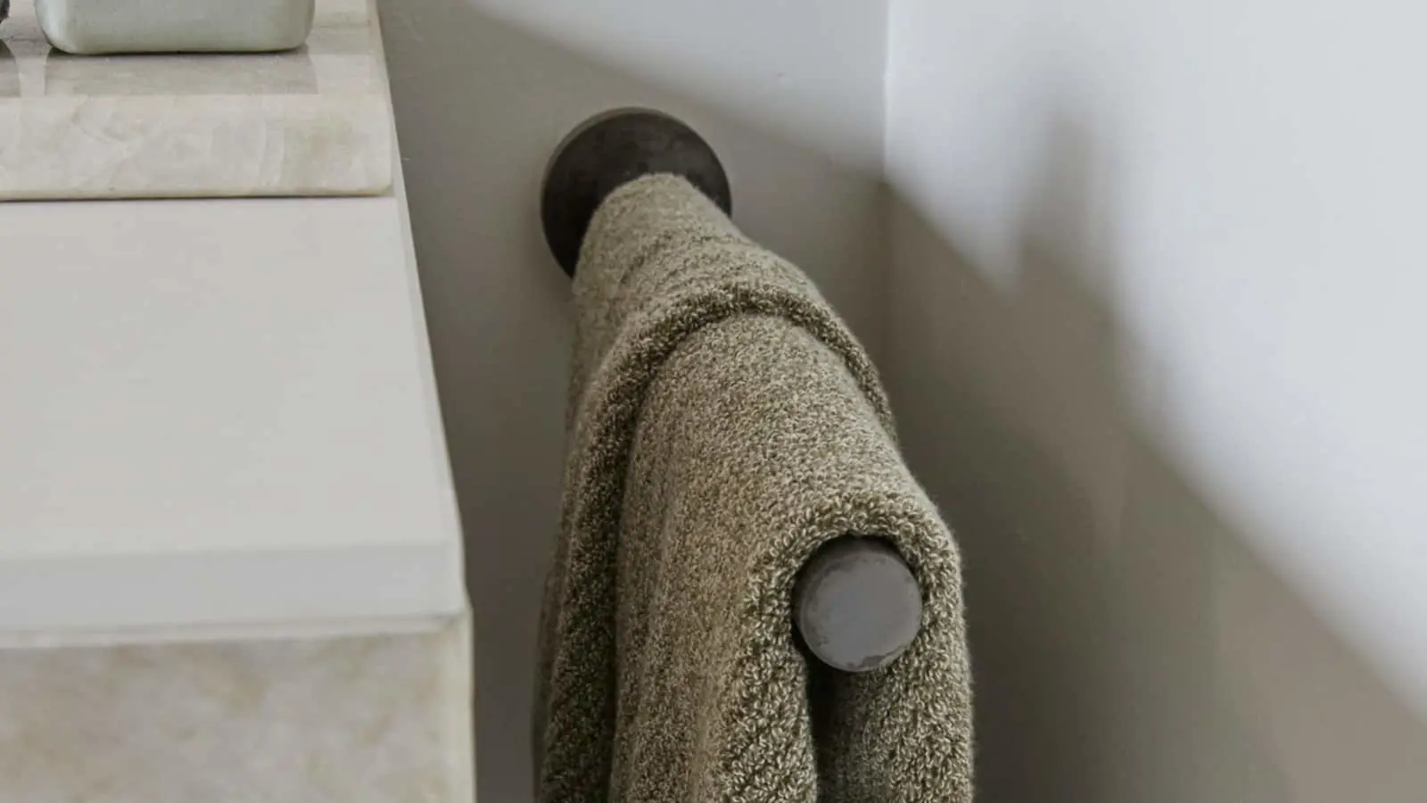 Beige towel hanging on a dark wall-mounted hook in a bathroom, next to a white countertop or shelf.